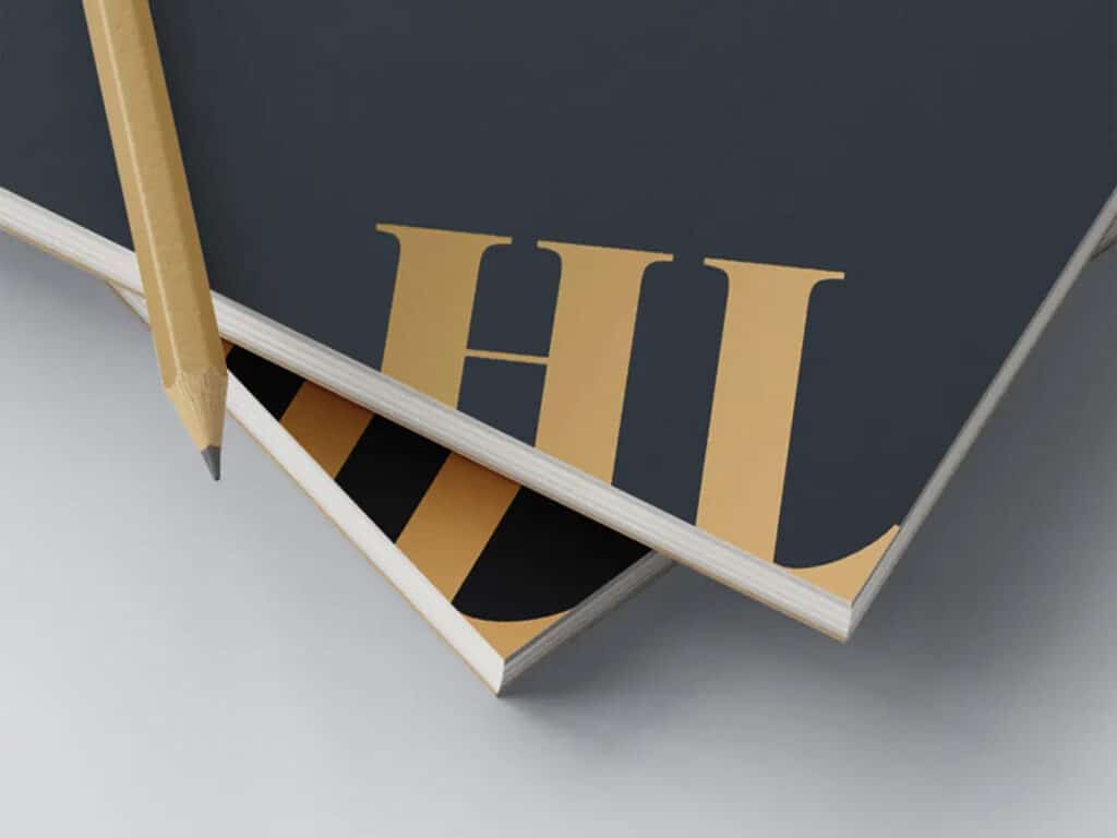 Boekje van donkerblauw papier met goudfolie en gestanste ‘HL’-initialen, gepresenteerd op een minimalistische ondergrond