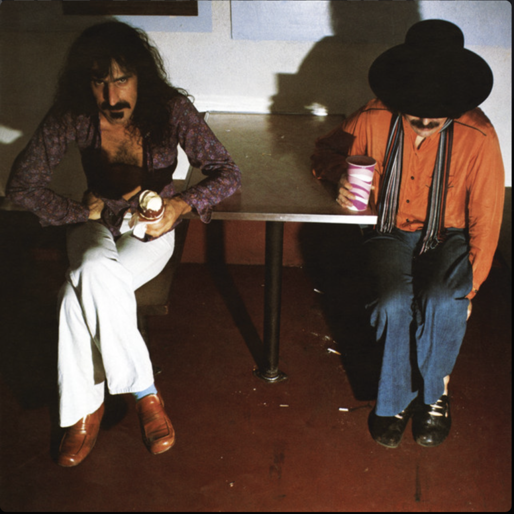 Frank Zappa en Captain Beefheart zittend aan een tafel op de albumcover van 'Bongo Fury', met Zappa die een muffin vasthoudt.
